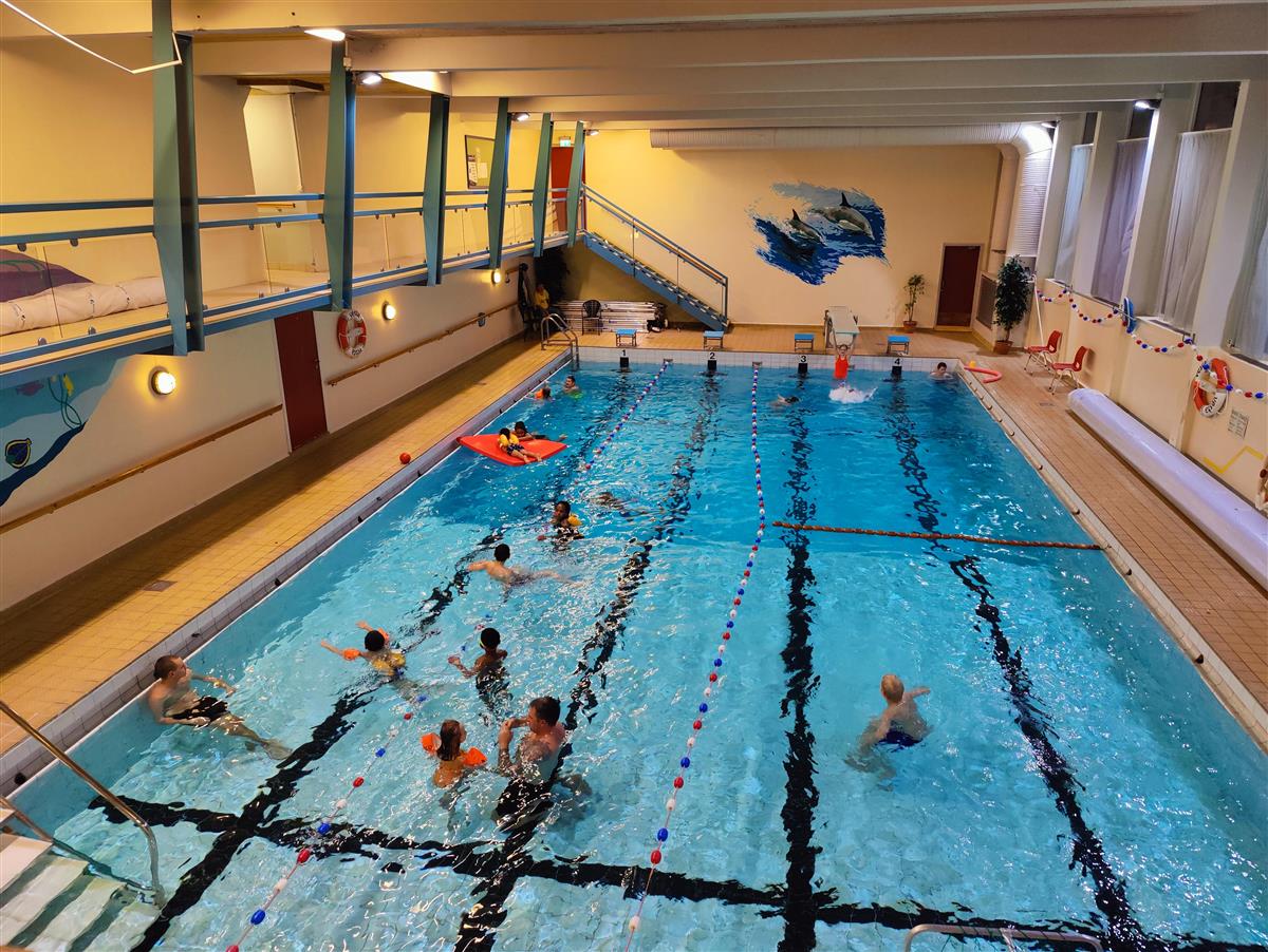 Et bilde som viser bassenget i Tingvoll svømmehall med mange badeglade publikummere i, store og små.  - Klikk for stort bilde